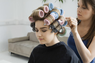 View of a cropped stylist fixing rollers in female model's hair 