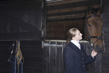 Young female horseback rider with horse in the stable