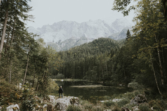 .Woman standing at a lake in the mountains surrounded by forest at daytime