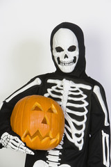Portrait of a kid wearing skeleton costume holding Jack-O-Lantern isolated over white background