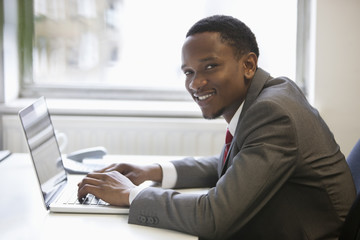 Fototapeta na wymiar Portrait of happy African American businessman using laptop at office desk