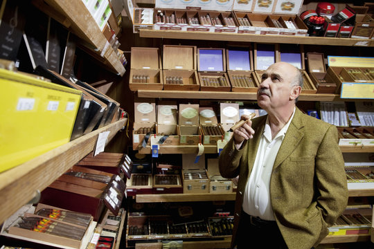 Small Tobacco Store Owner Looking At Cigar Boxes On Display In Shop