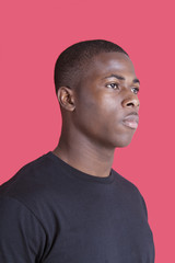 Serious African American young man looking away over pink background
