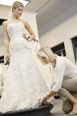 Fototapeta premium Senior employee adjusting wedding dress of beautiful young bride in bridal store