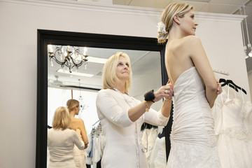 Senior owner assisting young bride getting dressed in wedding gown