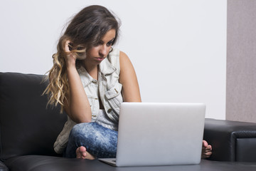Young creative woman sitting on a couch with laptop. Casual blogger woman.