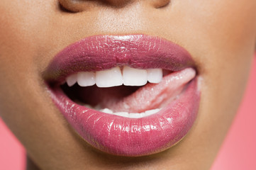 Cropped image of woman licking pink lipstick