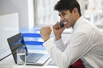 Excited businessman using cell phone at office desk