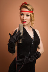 Pretty actress in black retro dress singing with microphone