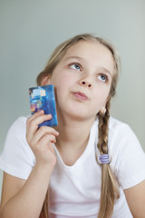 Thoughtful young girl holding credit card over gray background