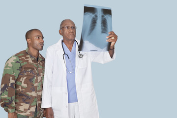Senior doctor with US Marine Corps soldier looking at x-ray report over light blue background