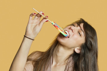 Portrait of a young woman eating lollipop over colored background