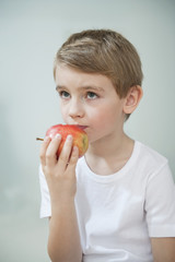 Portrait of young boy eating an apple over gray background