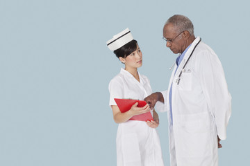 Two medical professionals in discussion over medical report against light blue background