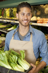 Happy young sales clerk holding bok choy in supermarket