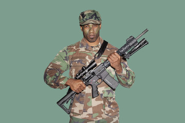 Portrait of a young African American US Marine Corps soldier with M4 assault rifle over green...