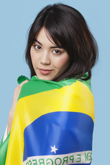 Patriotic young woman wrapped in Brazilian flag over blue background