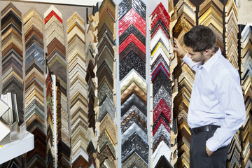 Side view of a young man browsing at a frame store with hands in pockets