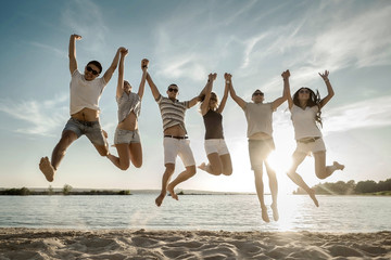 Friends jumping on the beach under sunset sunlight.