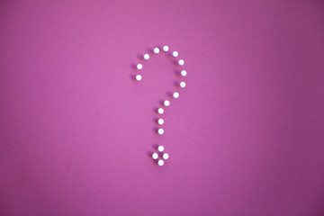 Close-up of push pins forming question mark over pink background