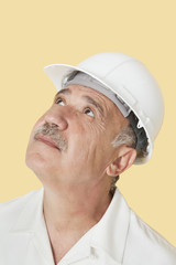 Senior man with hardhat looking up over yellow background