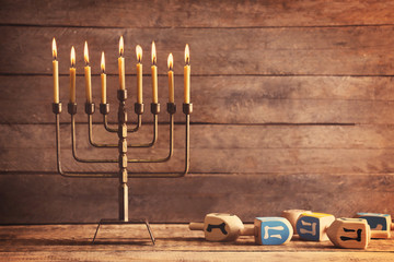 Menorah with candles for Hanukkah on table against wooden background