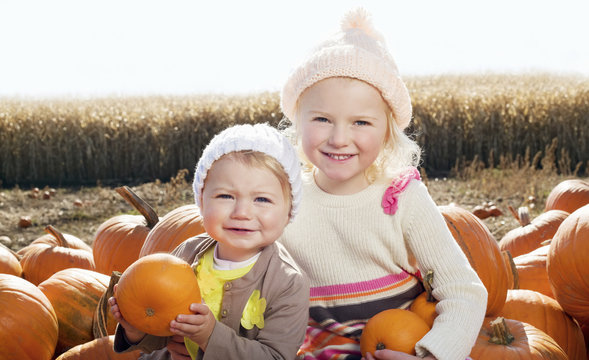 Portrait of sisters with pumpkin sitting on farm