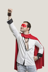 Fototapeta na wymiar Young man in superhero costume with hand raised against gray background