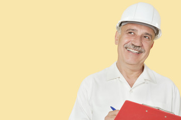 Senior constructor with clipboard looking away over yellow background