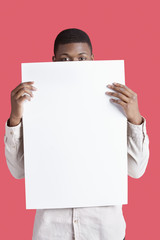 Portrait of a young man holding blank cardboard in front of face over pink background