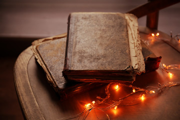 Old books and garland on wooden chair, closeup