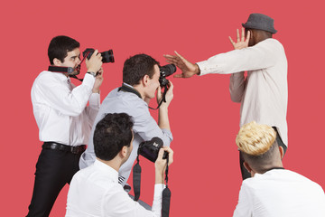 Young male celebrity shielding face from photographers over red background