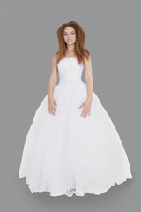 Portrait of elegant young brunette in wedding dress standing over gray background