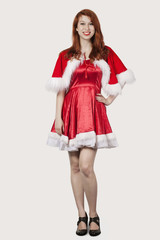 Portrait of happy young woman in Santa costume standing against gray background