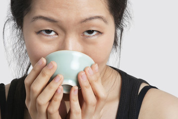 Portrait of a young woman drinking from bowl over light gray background