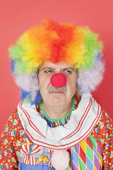Senior male clown frowning over red background