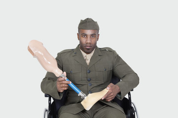 Portrait of US military officer in wheelchair holding prosthesis foot over gray background