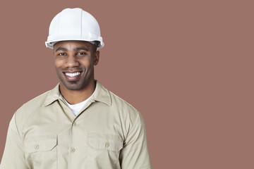 Portrait of happy young construction worker with hardhat over brown background