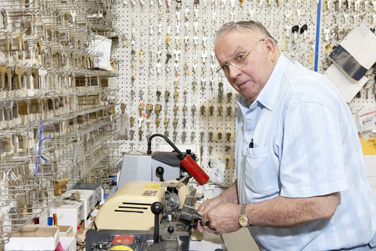 Senior Locksmith Looking Away While Making Key In Store