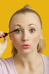 Obraz na płótnie Canvas Portrait of a beautiful young woman applying mascara over yellow background