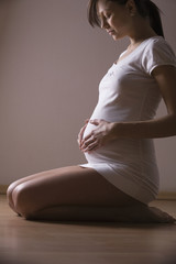 Full length side view of pregnant woman kneeling while holding stomach at home