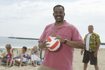 Portrait of an African American man holding volley ball with friends grouped behind at beach
