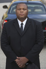 Portrait of mixed race serious male chauffeur with car in background