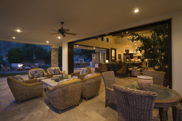 Wicker furniture in lit spacious home with porch view at night