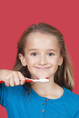 Portrait of girl holding toothbrush against red background