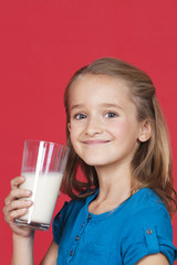 Portrait of young girl holding glass of milk against red background