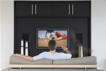 Back view of mid-adult man changing channels with television remote control in living room