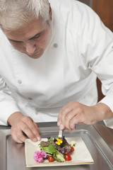 Obraz na płótnie Canvas Male chef arranging edible flowers on salad in commercial kitchen