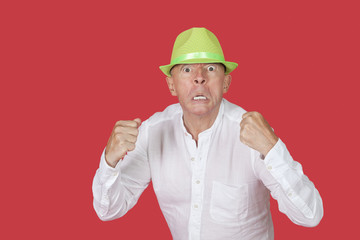 Portrait of an angry senior man clenching fists against red background