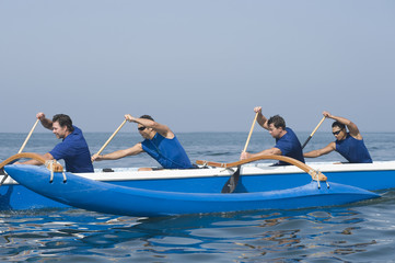 Side view of male rowers paddling outrigger canoe in race